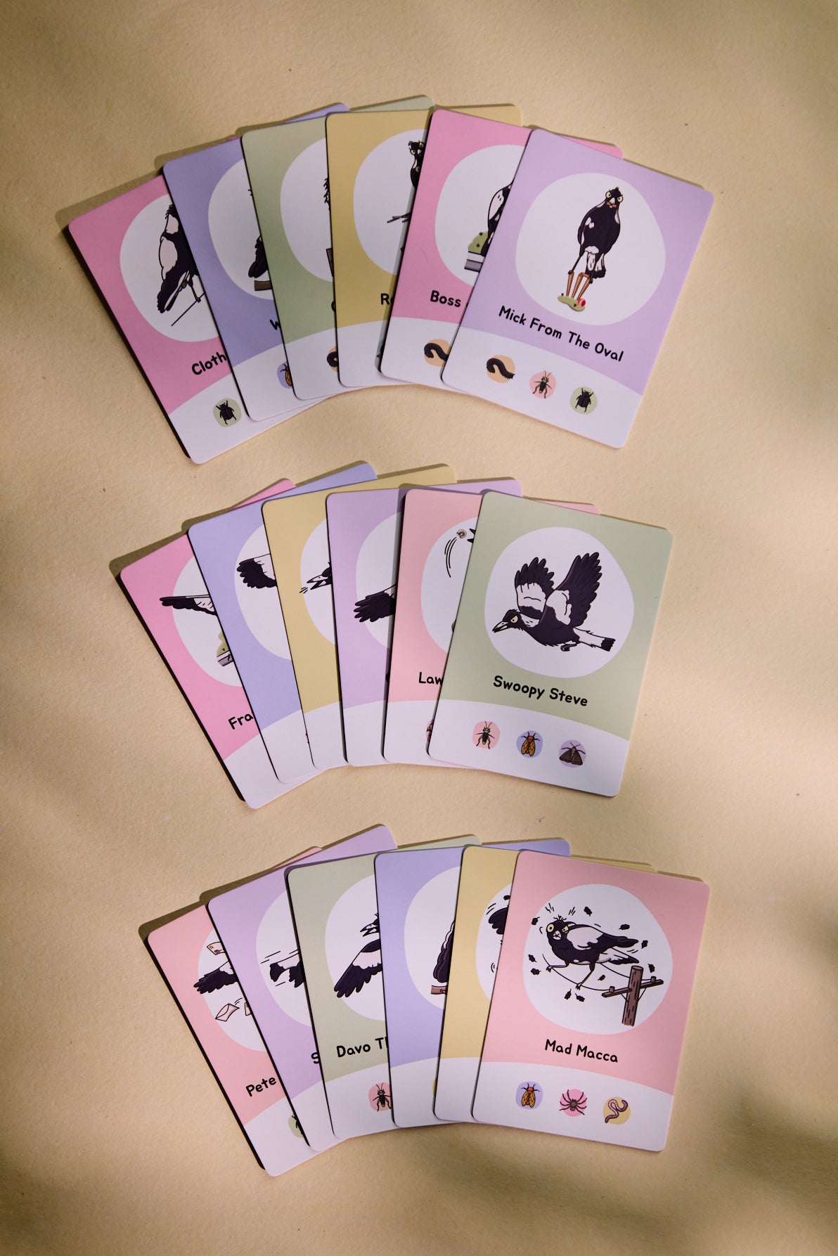 Three fanned decks of magpie cards on a beige surface, showing pastel pink, lavender, yellow, green, and white cards. 
